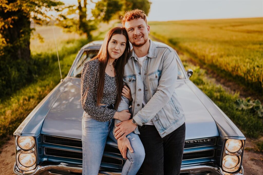 Młoda para siedząca na pontiacu w tle zachodzącego słońca – niezapomniana chwila pełna miłości i klasy
