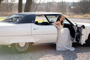 Uśmiechnięta panna młoda wychodząca z retroauta do ślubu Oldsmobile Ninety-Eight